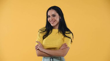 Cilveli, neşeli kadın kollarını kavuşturmuş kameraya gülümserken sarıya izole edilmiş.