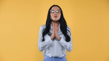 positive businesswoman with praying hands looking away isolated on yellow clipart