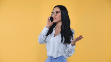 Gülümseyen iş kadını cep telefonuyla konuşurken sarıda izole bir şekilde işaret veriyor.