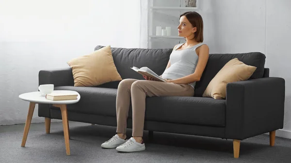 Dreamy Pregnant Woman Looking Away While Sitting Couch Book — Stock Photo, Image