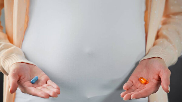 partial view of pregnant woman holding pills near belly