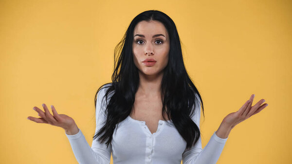 растерянная женщина пожимает плечами, глядя на камеру, изолированную на желтый