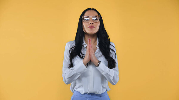 positive businesswoman with praying hands looking away isolated on yellow