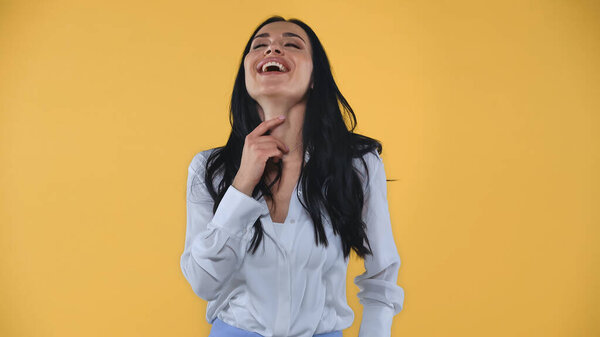 excited businesswoman touching neck while laughing with closed eyes isolated on yellow
