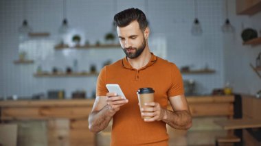 Sakallı adam kafeye gitmek için akıllı telefon ve kahve kullanıyor.