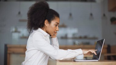 Afro-Amerikalı bir kadının akıllı telefondan konuşmasının ve kafedeki dizüstü bilgisayarı göstermesinin yan görüntüsü. 