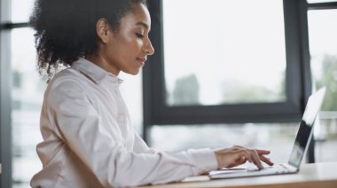 Laptop klavyesinde yazı yazan Afro-Amerikan kadının yan görüntüsü 