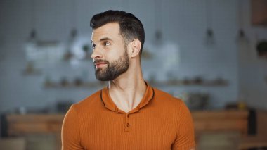 Turuncu tişörtlü sakallı bir adam kafeye bakıyor.