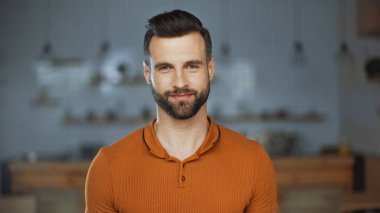 Kafede kameraya bakan turuncu tişörtlü neşeli bir adam.