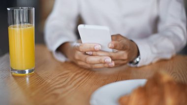 Portakal suyu yakınında akıllı telefondan yazı yazan Afro-Amerikan kadının kısmi görüntüsü