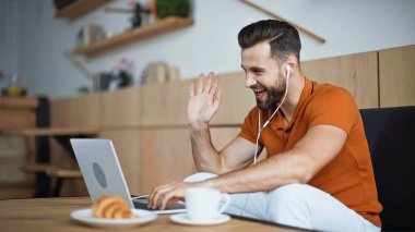 Kulaklıklı mutlu adam kafede video görüşmesi yapıyor.