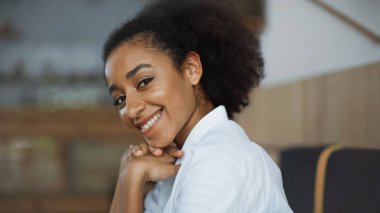 Mutlu Afro-Amerikalı kadın gülümsüyor ve kafede kameraya bakıyor.