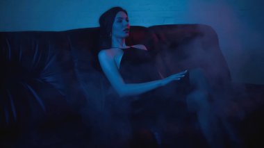 Siyah kanepede oturan esmer kadın dumanlı.