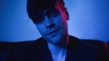 Ceketli adam mavi kameraya bakıyor. 