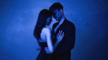 Siyah elbiseli seksi kadın mavi ceketli adamı kucaklıyor.