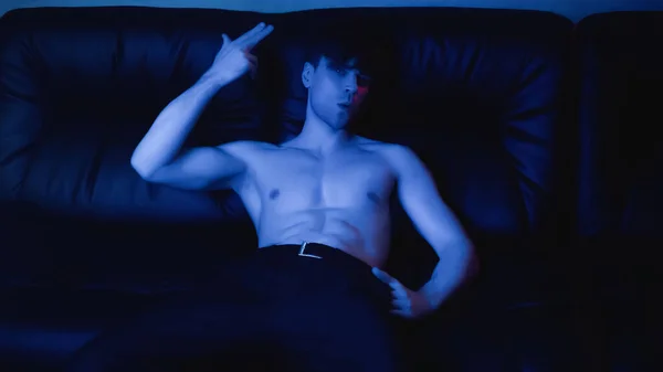 在黑色沙发上 穿着裤子摆出姿势 摆出姿势 赤身裸体男子身上的蓝色灯光 — 图库照片