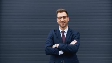 Kollarını kavuşturup gülümseyen takım elbiseli mutlu iş adamı.