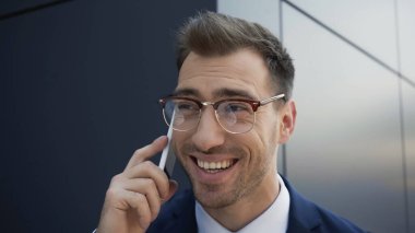 Gözlüklü neşeli işadamı binanın yakınında cep telefonuyla konuşuyor. 