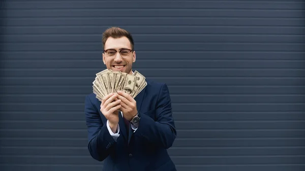rich businessman in suit smiling while holding dollars