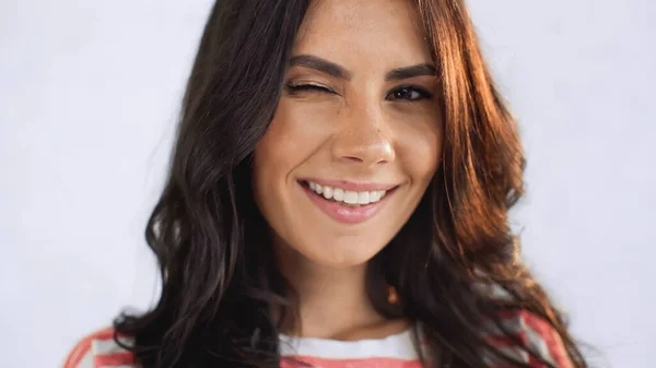 close up of cheerful and brunette woman winking eye while looking at camera