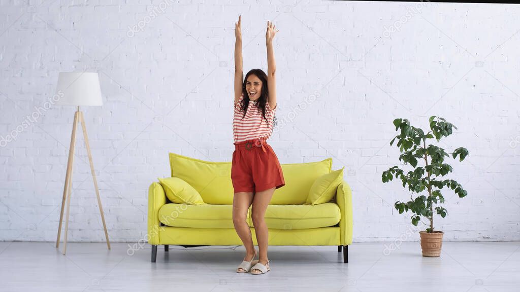 happy woman dancing near sofa in modern living room