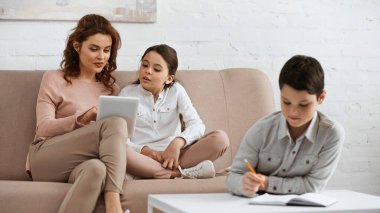Kızın ve oğlunun yanında dijital tablet kullanan kadın ön plan bulanıklığı üzerine ödev yapıyor. 