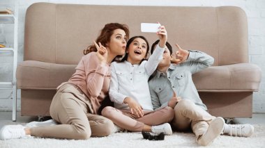 KYIV, UKRAINE - 15 Nisan 2019: Aile evdeki yerde joystick 'in yanında akıllı telefondan selfie çekiyor 