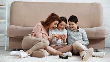 KYIV, UKRAINE - 15 Nisan 2019: Zeminde joystick 'in yanında akıllı telefon kullanan pozitif aile 