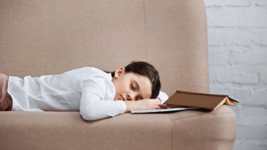 Kitap ve defterin yanındaki kanepede uyuyan kız. 