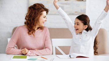 Neşeli çocuk dijital tablet ve kırtasiyenin yanında annesine bakıyor. 