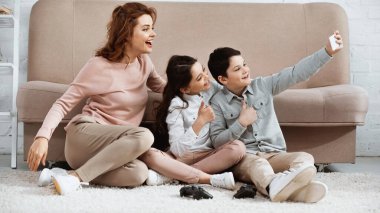 KYIV, UKRAINE - 15 Nisan 2019: Gülümseyen çocuklar annelerinin yanında selfie çekerken ve yerde joystick çekerken evet işareti yapıyorlar 