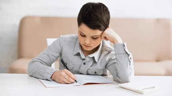 Niño Escribiendo Cuaderno Cerca Calculadora Mesa Casa —  Fotos de Stock