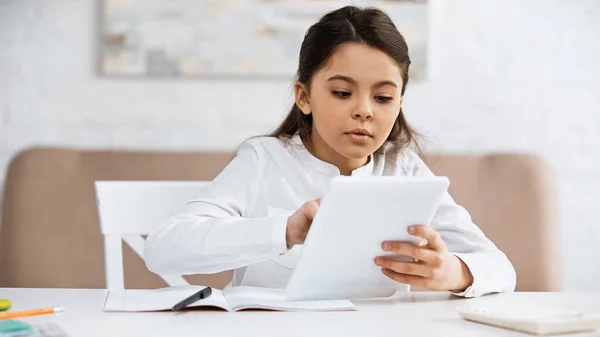 Girl using digital tablet near notebook and blurred calculator