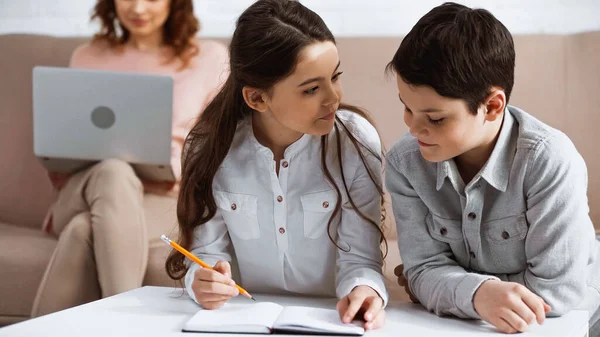 Kinder Mit Notizbuch Bei Hausaufgaben Während Mutter Laptop Auf Verschwommenem — Stockfoto