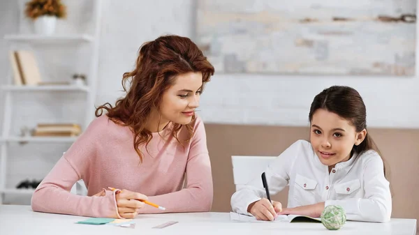 Menina Sorridente Escrevendo Caderno Perto Mãe Com Lápis Casa — Fotografia de Stock