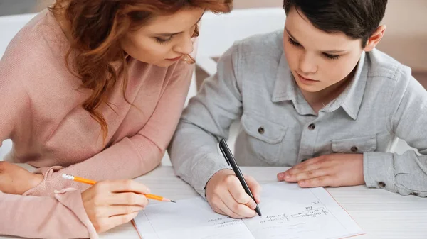 Frau Hält Bleistift Neben Frühem Sohn Und Schreibt Auf Notizbuch — Stockfoto