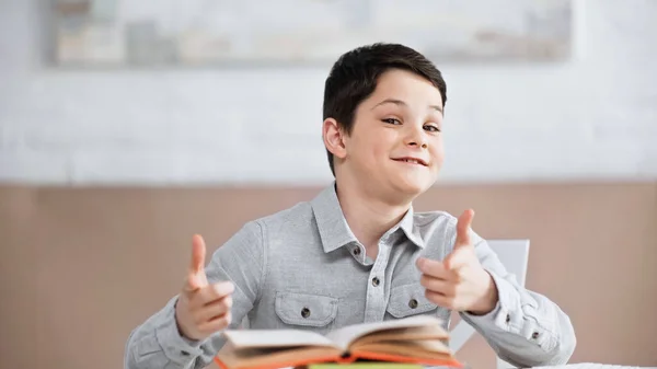 Smiling Boy Pointing Camera Book Blurred Foreground Home — Stock Photo, Image