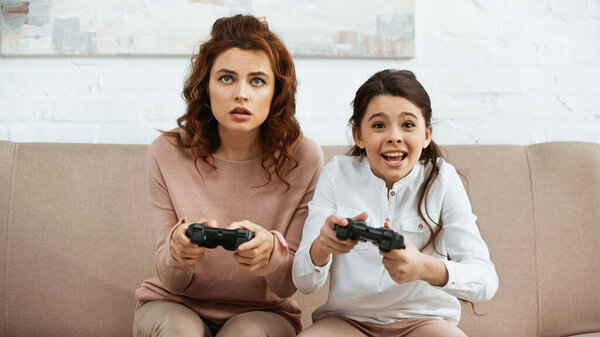 KYIV, UKRAINE -  APRIL 15, 2019: Cheerful kid playing video game with mother at home 