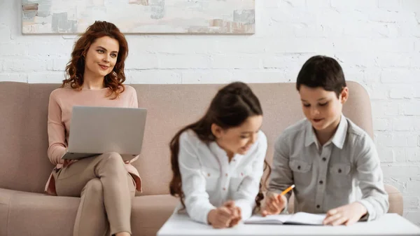 Mujer Con Portátil Mirando Los Niños Con Cuaderno Haciendo Tarea — Foto de Stock