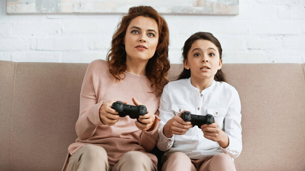 KYIV, UKRAINE -  APRIL 15, 2019: Focused mother and daughter playing video game at home 