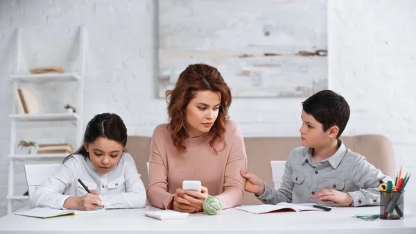 Frau Mit Handy Hilft Kindern Bei Hausaufgaben Tisch — Stockfoto