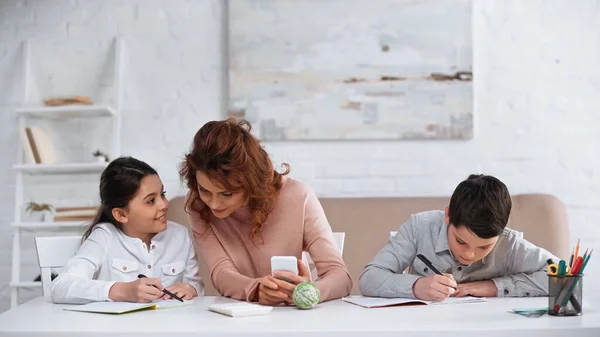 Smiling Kid Talking Mother Smartphone While Brother Doing Homework — Stock Photo, Image