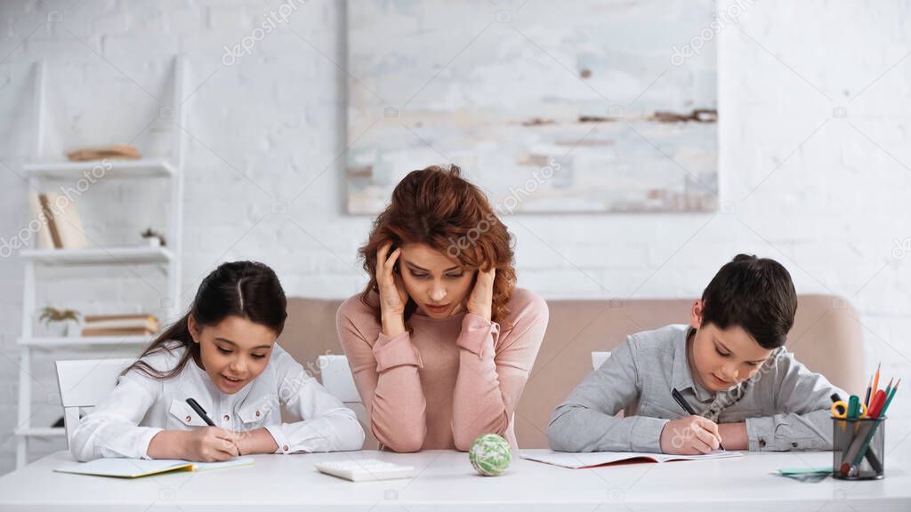 Woman sitting near children writing on notebooks during homework 