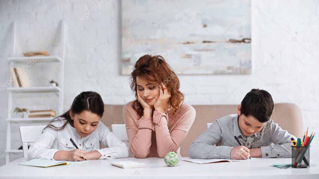 Mother supporting kids writing on notebooks during homework 