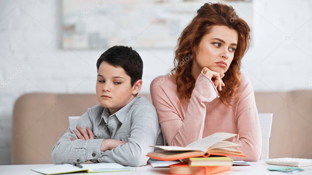 Sad mother and kid sitting near books on blurred foreground at home 