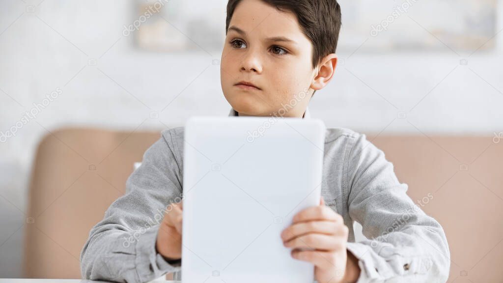 Preteen boy holding digital tablet on blurred foreground during online education 