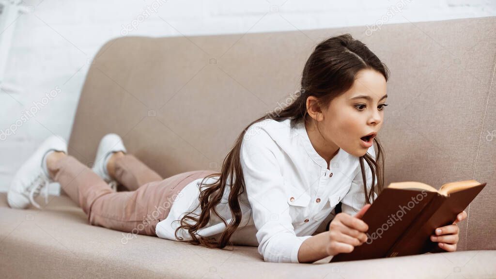 Amazed preteen girl reading book on couch 