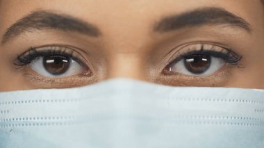 Tıbbi maskeli Afrikalı Amerikalı doktorun kameraya baktığı yer.