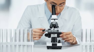 Laboratuvardaki test tüplerinin yakınındaki mikroskoptan bakan Afrikalı Amerikalı bilim adamı. 