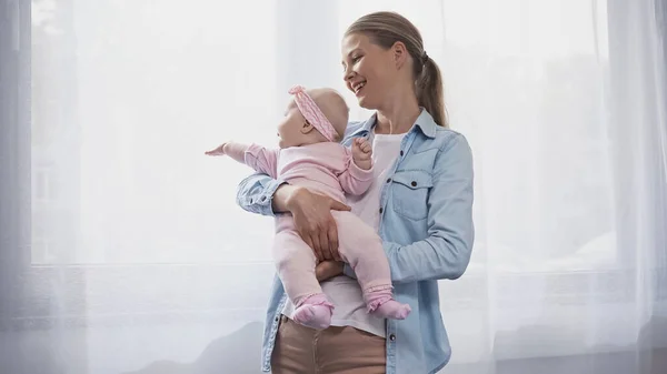 Alegre Madre Sosteniendo Brazos Bebé Hija Señalando Con Mano Ventana — Foto de Stock